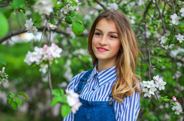 Pretty teen girl are posing in garden near blossom tree with white flowers. Spring time