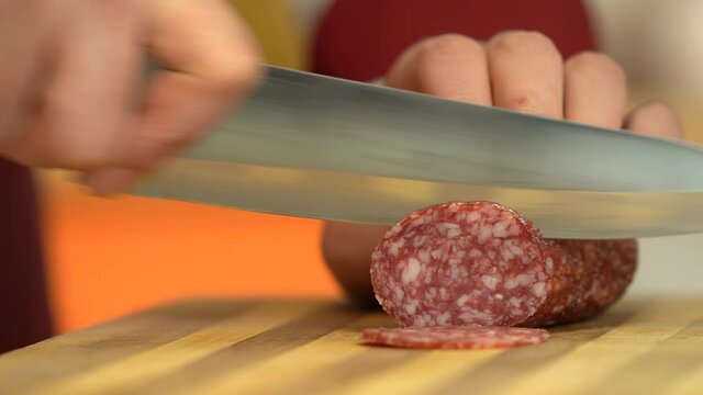   Chef is slicing with sharp knife the  salami sausage in kitchen. Close view man cutting salami sausage. 