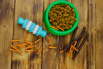 Dog toy, delicacy food and feed for dogs in green plastic bowl on wooden background. Top view. Dog care concept