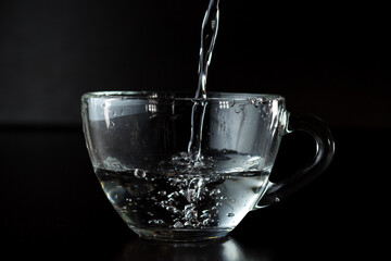 pouring water into a glass. transparent cup with water on a dark background.
