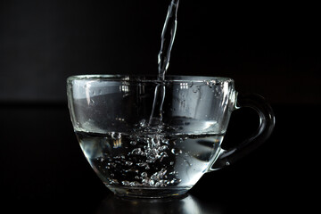 pouring water into a glass. transparent cup with water on a dark background.