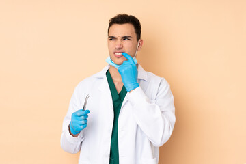 Young dentist man holding tools isolated on beige background nervous and scared