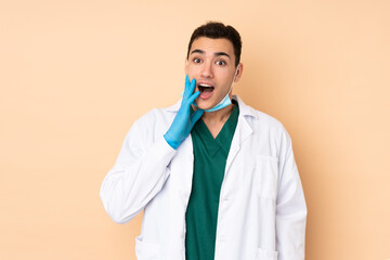 Young dentist man holding tools isolated on beige background with surprise and shocked facial expression