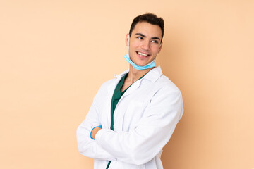 Young dentist man holding tools isolated on beige background with arms crossed and happy