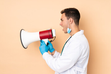 Young dentist man holding tools isolated on beige background shouting through a megaphone