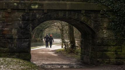 A couple taking a winter walk along the Leeds and Liverpool Canal glimpsed through the arch of a bridge