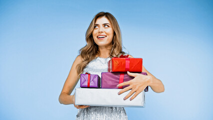Fototapeta premium happy woman with curly hair holding wrapped presents on blue