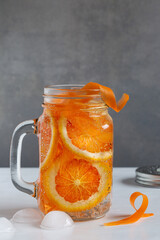 Offenes Henkelglas mit frisch gekühltem Vitaminwasser aus Blutorange und Karotte vor grauem...