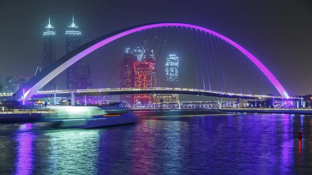Illuminated Pedestrian Bridge over the Dubai Water Canal night timelapse which links Dubai Creek to Jumeirah Beach weaving through Deira, Downtown Dubai and Safa Park. Skyscrapers skyline. Dubai