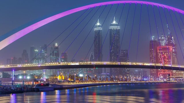 Illuminated Pedestrian Bridge over the Dubai Water Canal day to night transition timelapse which links Dubai Creek to Jumeirah Beach weaving through Deira, Downtown Dubai and Safa Park. Skyscrapers