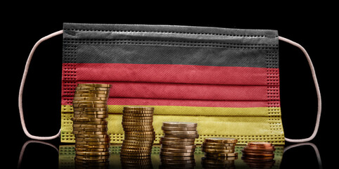 Medical mask with the flag of Germany behind some shrinking stacks of various coins.(series)