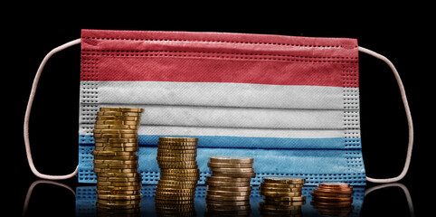 Medical mask with the flag of Luxembourg behind some shrinking stacks of various coins.(series)