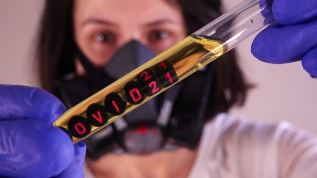 Caucasian Female Scientist Wearing Gas Mask and Blue Latex Gloves while Examining Test Tube With Covid-21 Sample
