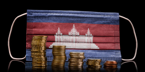 Medical mask with the flag of Cambodia behind some shrinking stacks of various coins.(series)