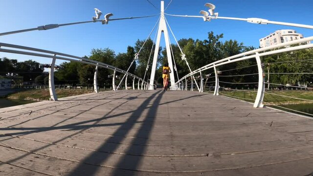 Rear view of woman riding electric scooter across bridge in Kharkiv Strelka park, Ukraine