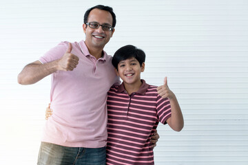 Happy Indian dad and son hugging and thumb up, smiling at camera on white wall