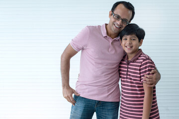 Naklejka premium Happy Indian dad and son hugging and smiling at camera on white wall