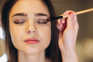 Portrait of a beautiful face of a woman with closed eyes and beautiful makeup. The makeup artist applies the eyeshadow to the eyes with a brush. shining eyeshadow