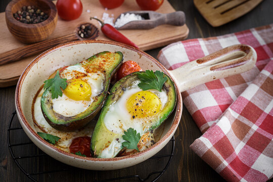 Avocado baked with egg on ceramic serving pan.