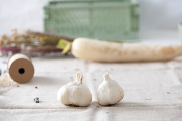 Garlic  on  bright blurred background,  organic beige linen , green crate , white radish and natural dried flowers.
