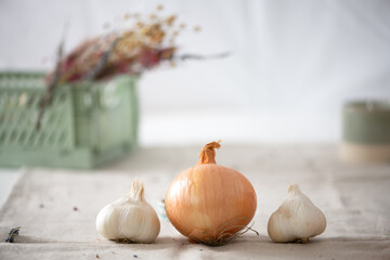 Garlic  and yellow onion .
In the  bright blurred background  you can find organic beige linen, green crate and dried flowers.
Desiged studio photography. Homely designed atmosphere.