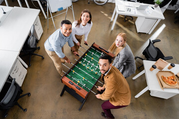 Overhead view of cheerful multiethnic business people playing table soccer near pizza in office
