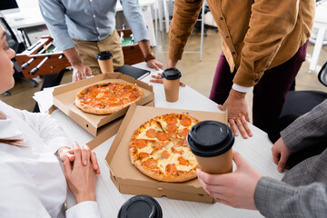 Businesswoman sitting near colleagues with takeaway drink and tasty pizza in office