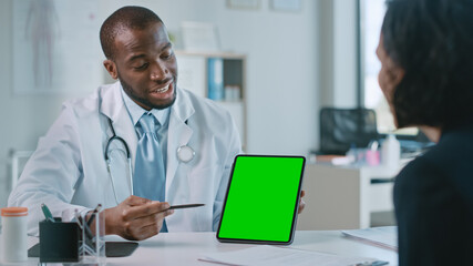African American Medical Doctor is Explaining Diagnosis to a Patient on a Tablet with Green Screen in a Health Clinic. Assistant in White Lab Coat is Reading Medical History in Hospital Office. 
