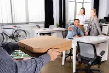 Delivery man holding takeaway pizza near business people on blurred background