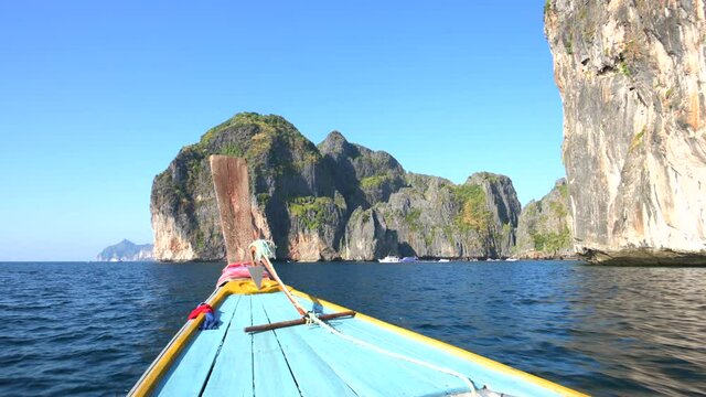 Stunning view of a longtail boat sailing on a blue water with some limestone krast in the distance. Maya Bay, Phi Phi Island, Phuket, Thailand.