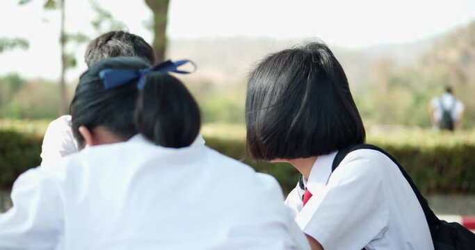 Back view of female Asian high school students in white uniform waiting for the school shuttle or waiting for their parents to pick them home in the evening after school.