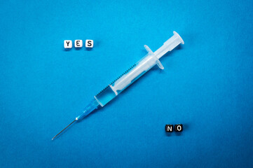 Yes No words made of square letters and a syringe on blue background. Pros and cons of coronavirus...
