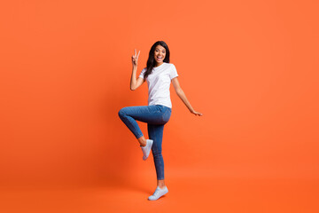 Fototapeta na wymiar Full length photo of lady show v-sign open mouth wear white t-shirt jeans footwear isolated orange color background
