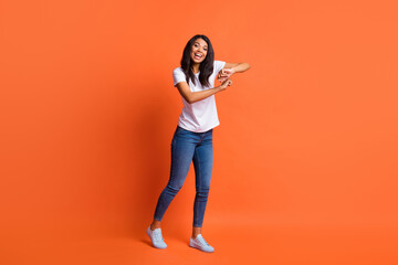 Full length photo of girl dance enjoy free-time wear white t-shirt jeans sneakers isolated orange color background