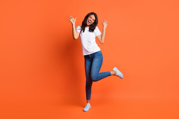 Full length photo of lady dance open mouth wear white t-shirt jeans sneakers isolated orange color background