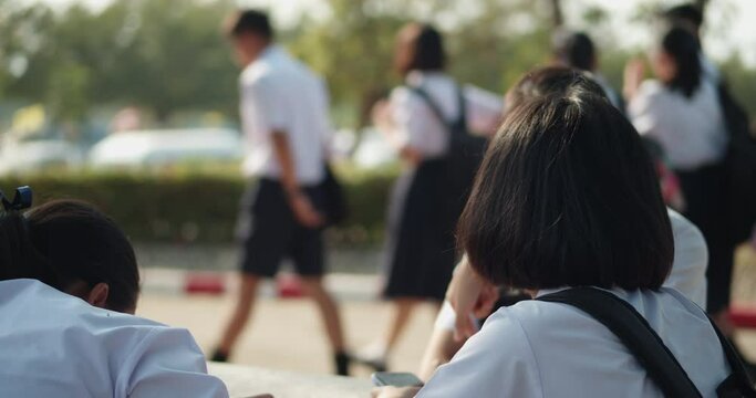 Back view of female Asian high school students in white uniform waiting for the school shuttle or waiting for their parents to pick them home in the evening after school.