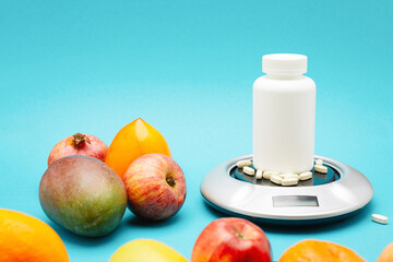 White bottle with pills on scales for food and near many different fruits isolated on blue...