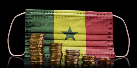 Medical mask with the flag of Senegal behind some shrinking stacks of various coins.(series)
