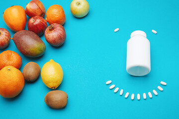 View from the top of white bottle with pills and many different fruits isolated on blue background.