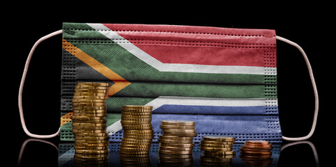 Medical mask with the flag of South Africa behind some shrinking stacks of various coins.(series)