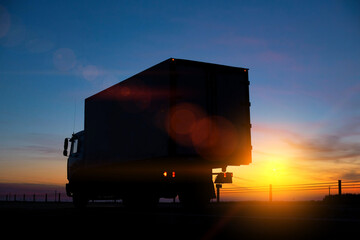Truck driver transports cargo on a truck against the backdrop of sunset at night. The concept of...
