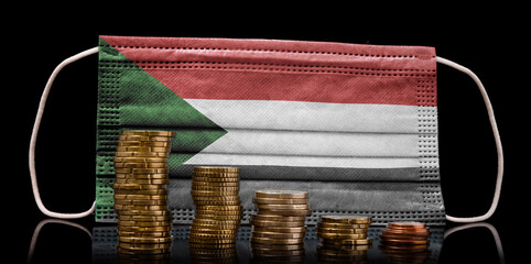 Medical mask with the flag of Sudan behind some shrinking stacks of various coins.(series)