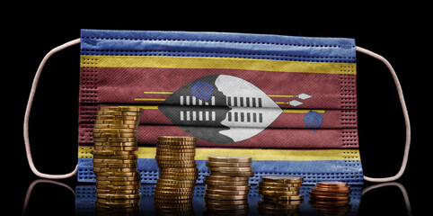 Medical mask with the flag of Swaziland behind some shrinking stacks of various coins.(series)