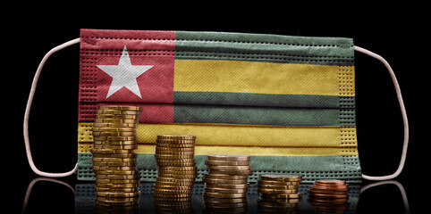 Medical mask with the flag of Togo behind some shrinking stacks of various coins.(series)