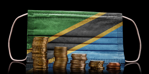 Medical mask with the flag of Tanzania behind some shrinking stacks of various coins.(series)