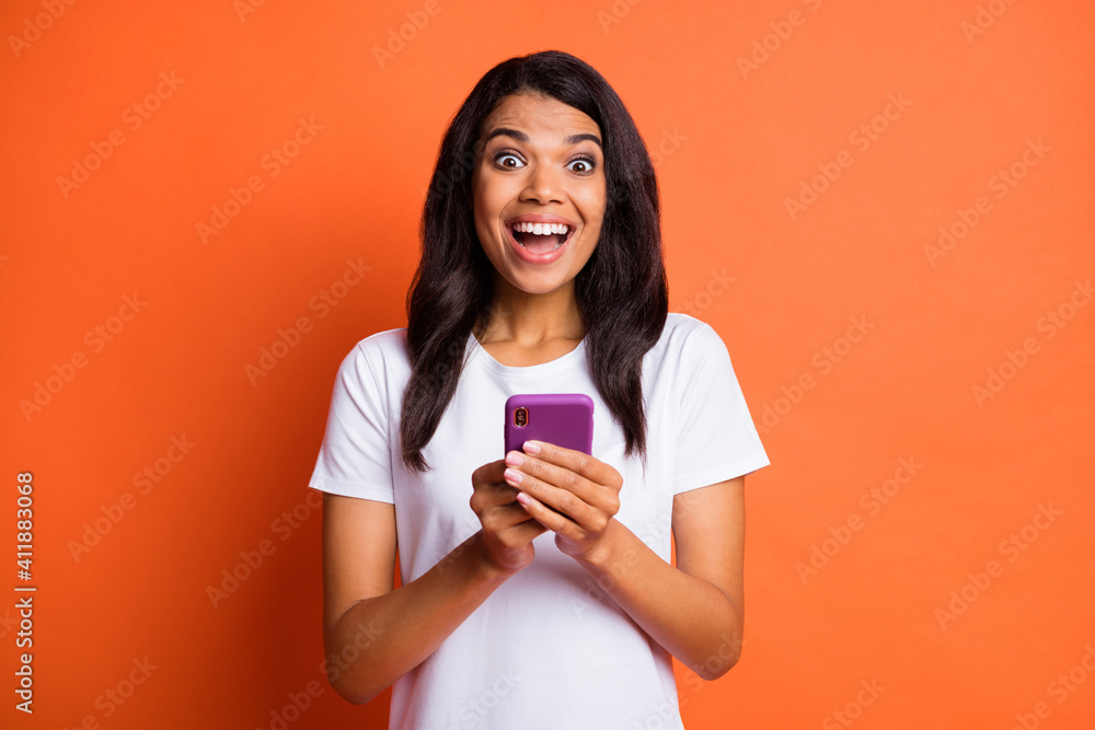 Wall mural Photo of excited crazy lady hold cellphone open mouth wear white t-shirt isolated orange color background