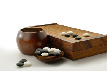 black and white stones of baduk game on wooden board showing white stones surrounding by group of black stones in the corner
