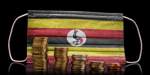 Medical mask with the flag of Uganda behind some shrinking stacks of various coins.(series)
