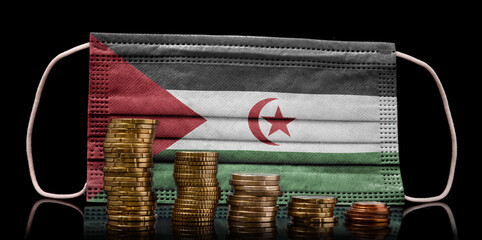 Medical mask with the flag of Western Sahara behind some shrinking stacks of various coins.(series)