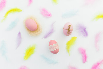 Ester composition with colorful eggs and pastel feathers on white background. Flat lay